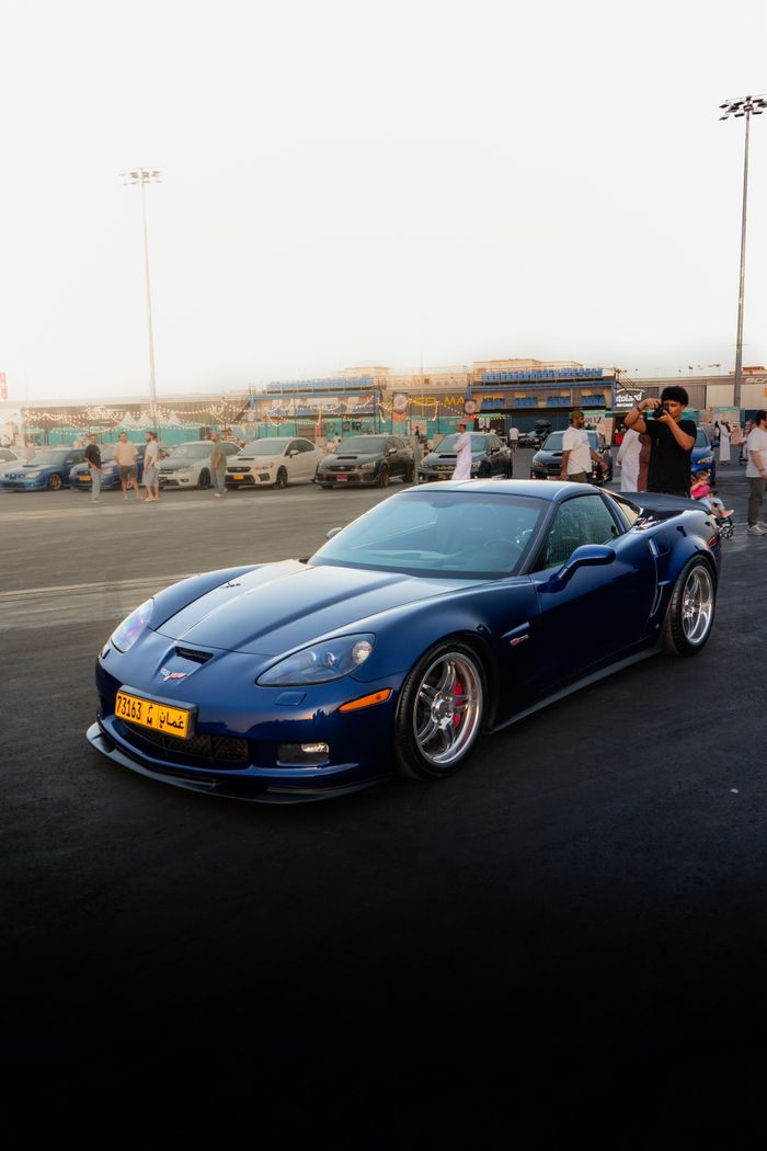 A striking blue sports car showcased at an outdoor auto event with spectators in the background.